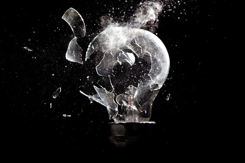 Close-up of light bulb breaking against black background