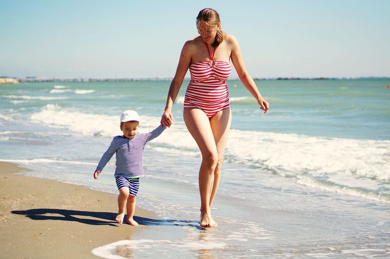 Full length of woman on beach with the child against sea