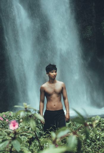 Shirtless man standing against waterfall in forest