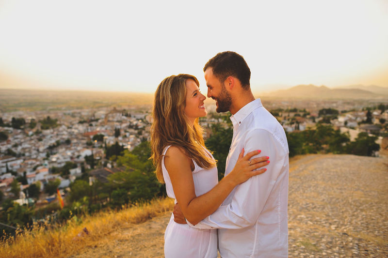 Happy romantic couple standing on cobbled road against sky during sunset