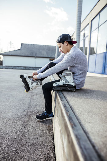 Young man sitting on ramp putting on inline skates
