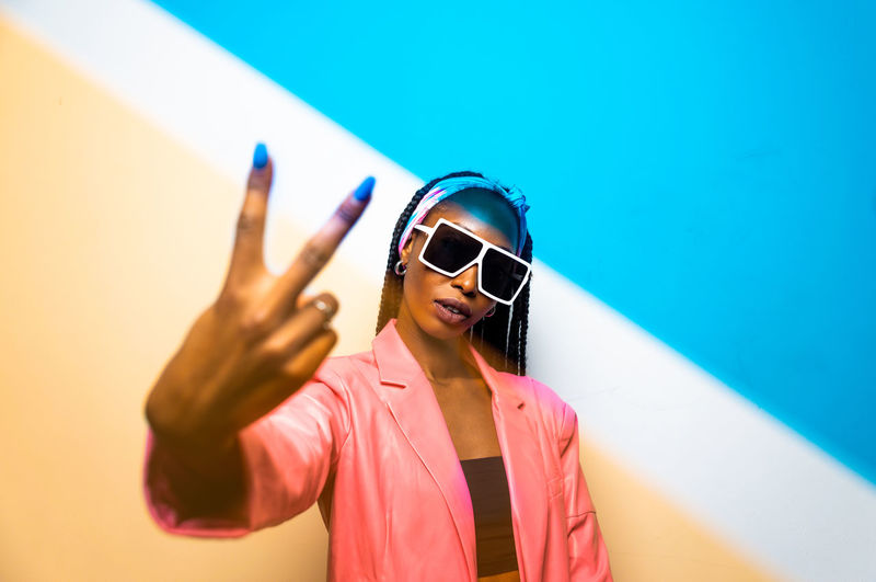 Portrait of woman wearing sunglasses standing against blue background