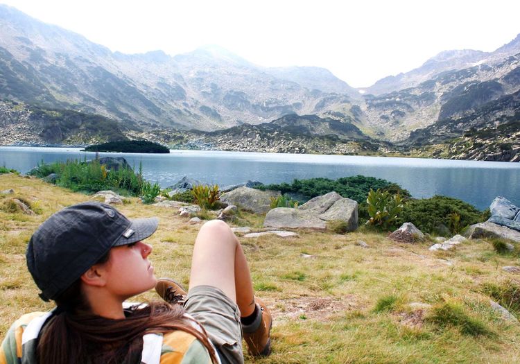 Young woman relaxing at grassy lakeshore against mountains