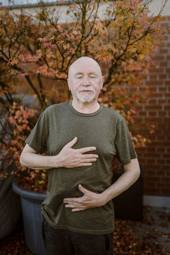 Senior man doing breathing exercise while standing against plant