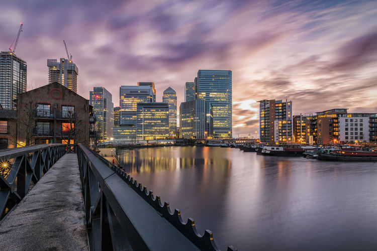 Illuminated buildings at waterfront against sky during sunset