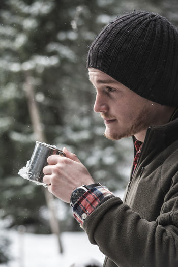 Side view of hiker drinking coffee standing on snow covered mountain against sky