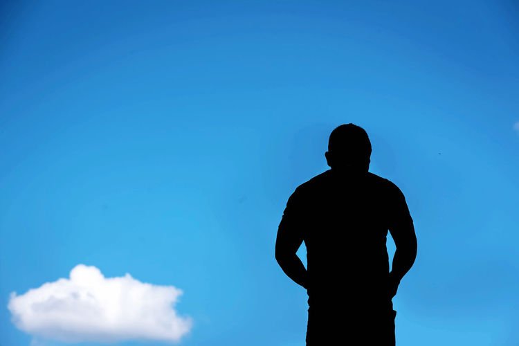 Rear view of silhouette man standing against blue sky
