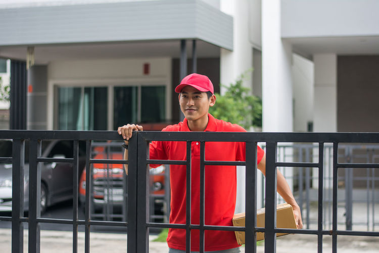 Delivery man standing at closed gate against buildings