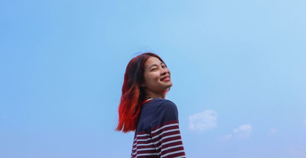 Smiling woman with dyed hair against blue sky