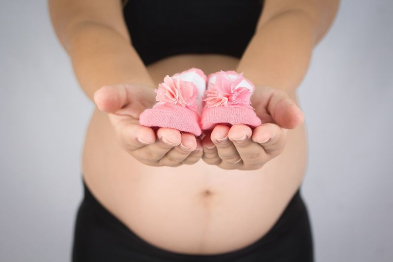 Midsection of pregnant woman holding baby booties over gray background