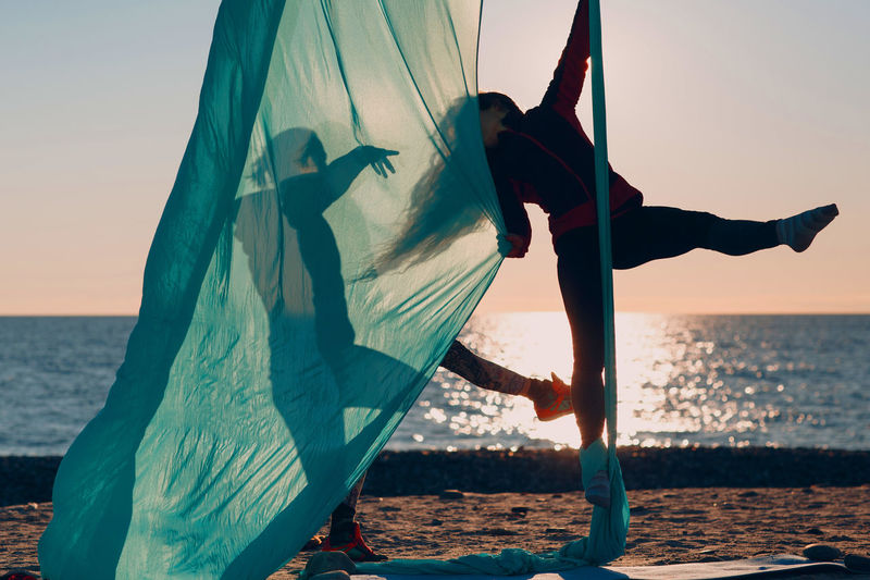 Full length of women dancing at beach against sky during sunset