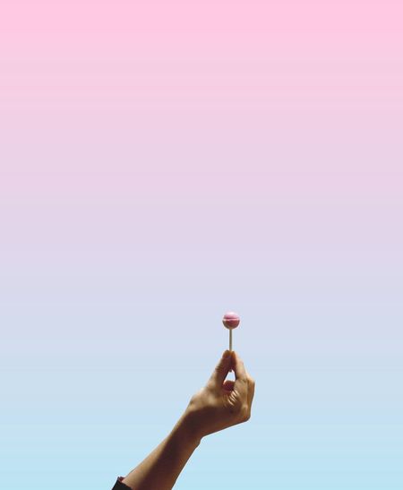 Cropped hand holding candy against colored background