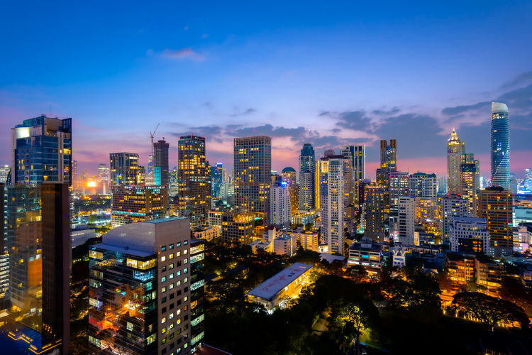 Illuminated modern buildings in city against sky at night