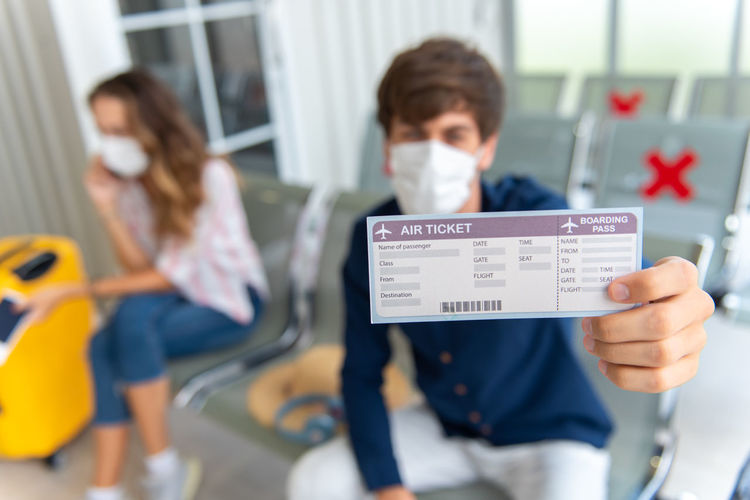 Focus on the boarding pass of caucasian man wear face mask traveling by airplane with his girlfriend 