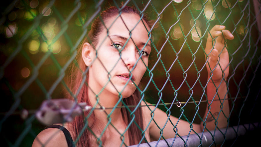 Close-up of young woman seen through chainlink fence