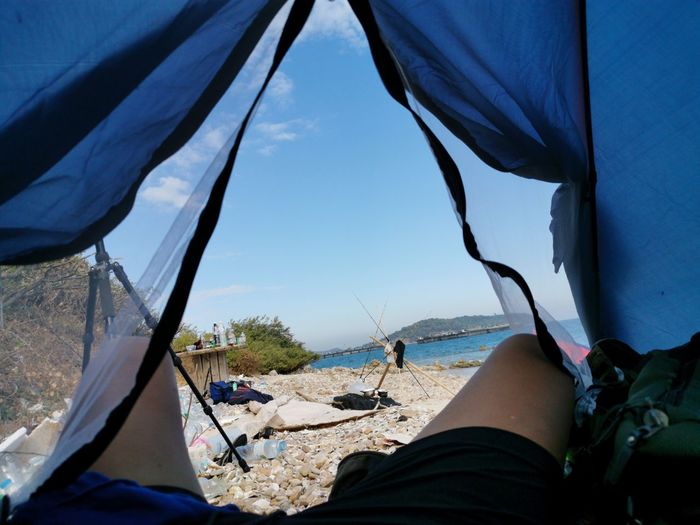 Low section of person in tent by sea against sky