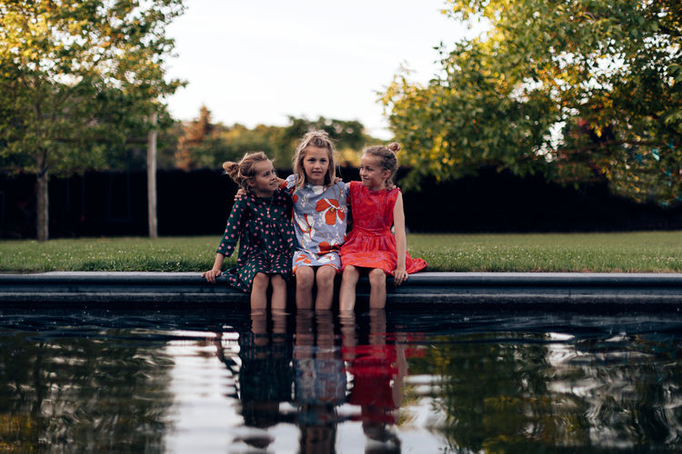 Three girls young child sisters with feet soaking in water on a late day of summer - friendship