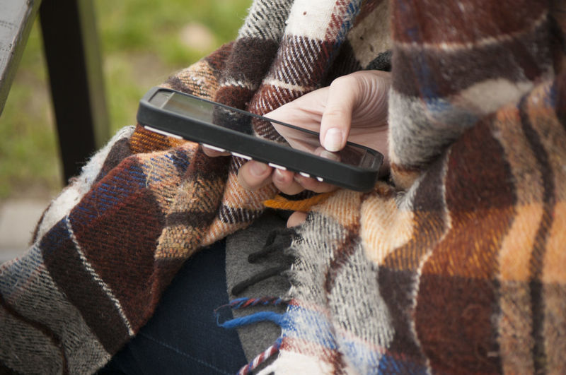 Midsection of woman with blanket using mobile phone outdoors