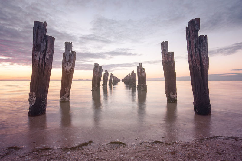 Wooden posts on beach against cloudy sky during sunset