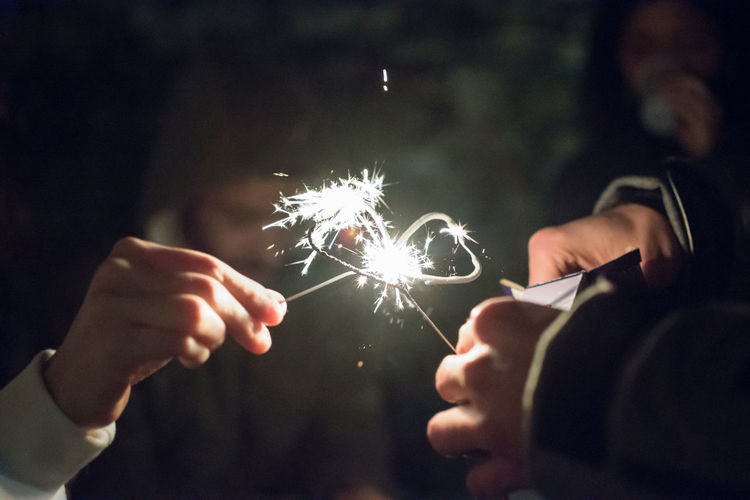 Cropped image of people holding sparkler at night
