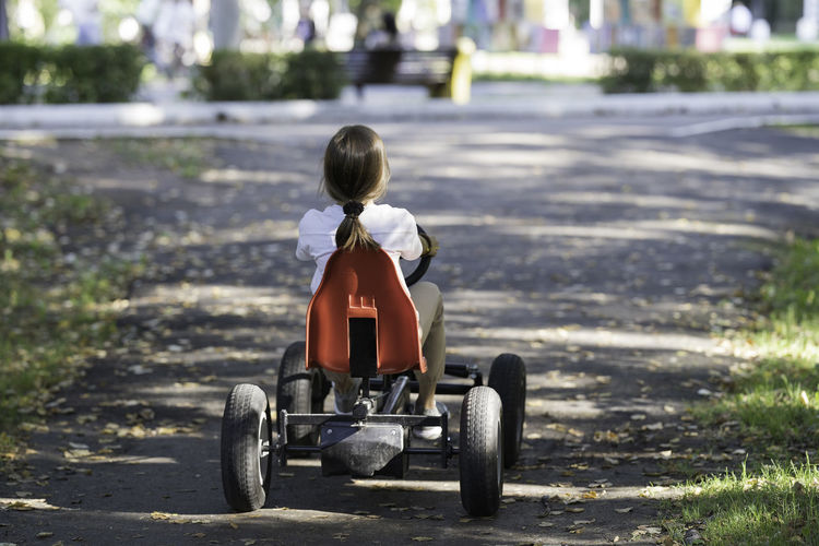 Rear view of boy riding toy car on road