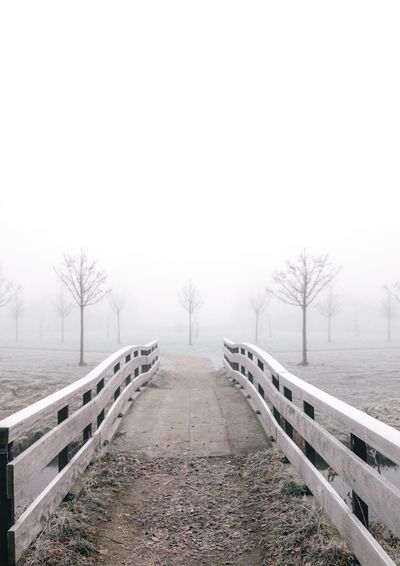 Footbridge on foggy landscape against sky