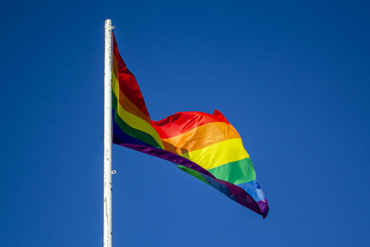 Low angle view of rainbow flag against clear blue sky