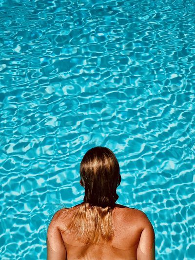 Rear view of shirtless woman against swimming pool