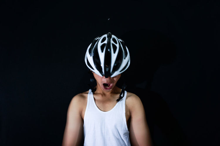Close-up of man yawning while wearing bicycle helmet against black background