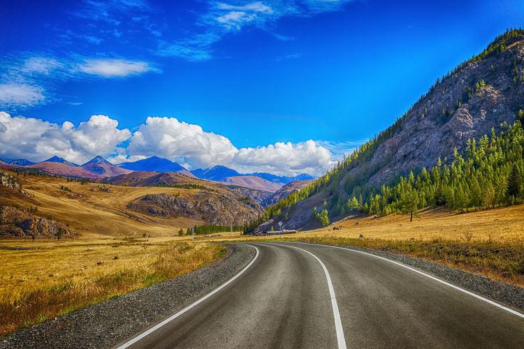 Road leading towards mountains against blue sky