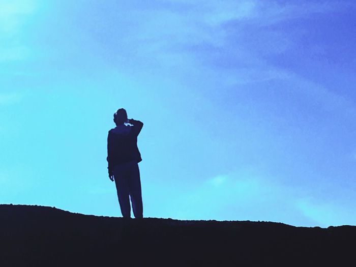 Silhouette of woman standing against blue sky