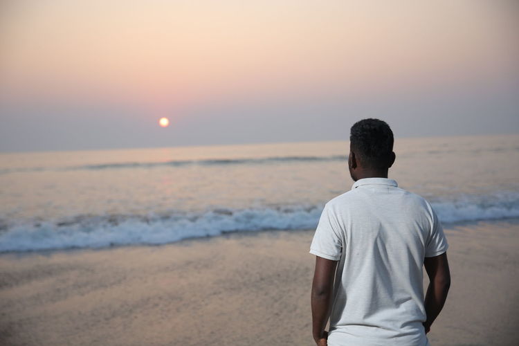 Rear view of man looking at sea during sunset