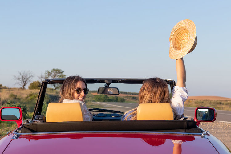 Back view of young girls on a red classic cabrio car looking at camera enjoying summer girls roatrip