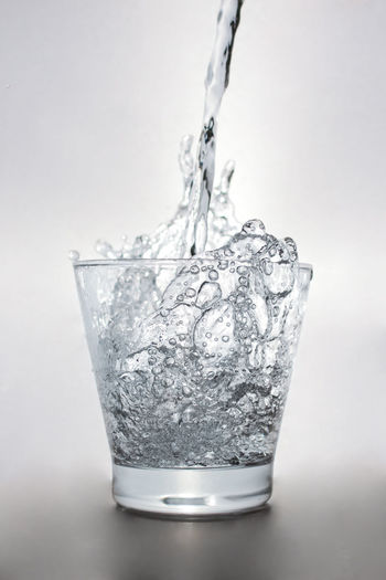Close-up of drink pouring water in glass against white background