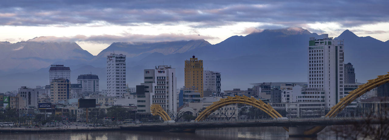 Bridge over river by buildings against sky in city