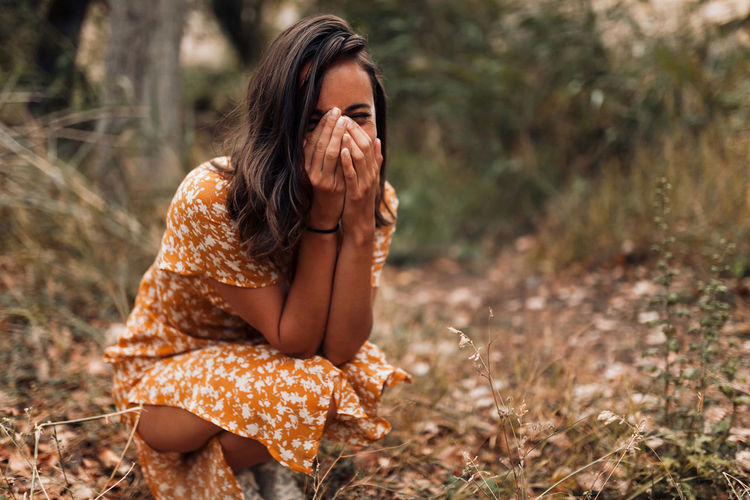 Young woman with hands covering mouth crouching in forest