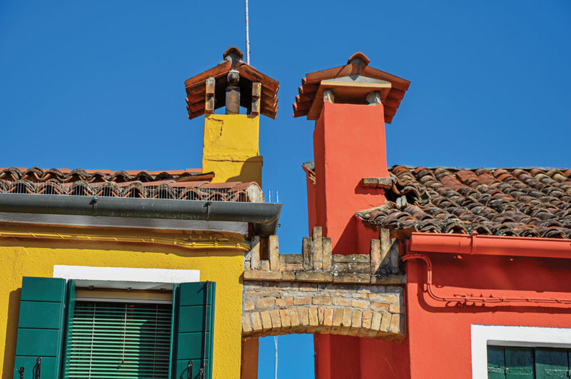 Chimneys and arch between colorful houses in burano, a gracious little town full of canals in italy.