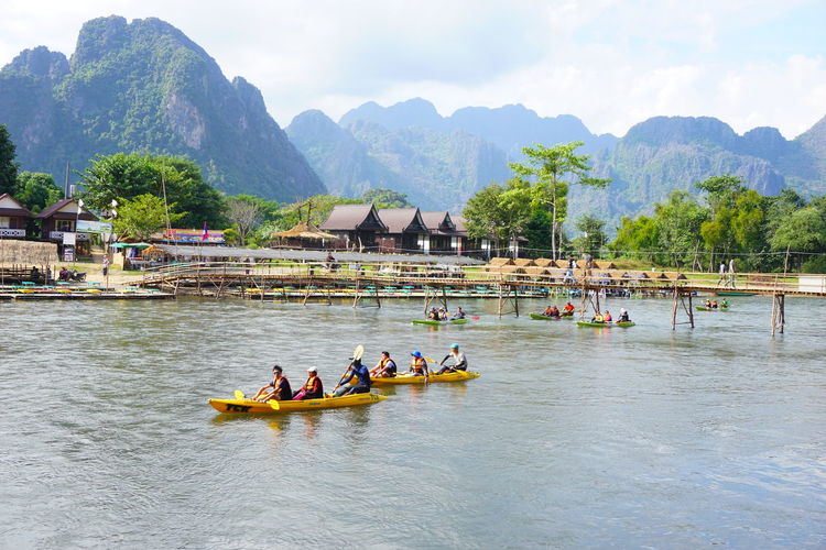 People kayaking in river against mountains
