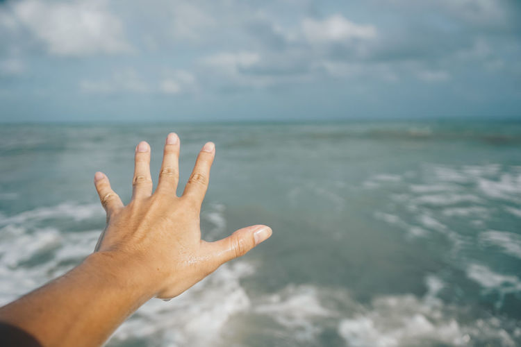 Cropped image of hand against sea against sky