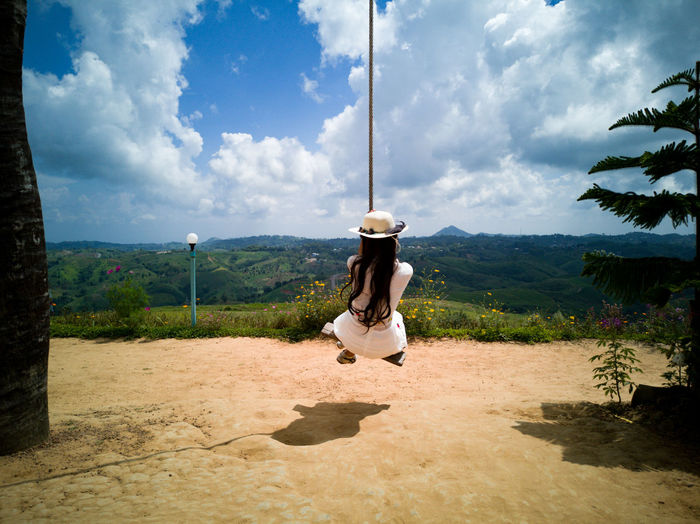 Rear view of woman swinging on rope swing against sky