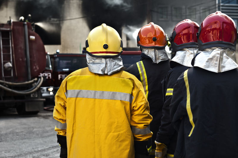 Rear view of firefighters wearing uniform standing on city street