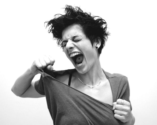 Woman screaming while tearing t-shirt against white background