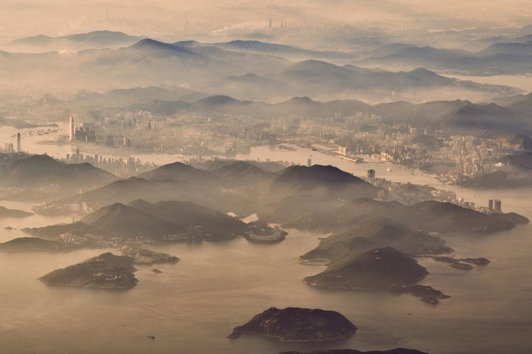 Aerial view of mountains in sea by buildings during sunset