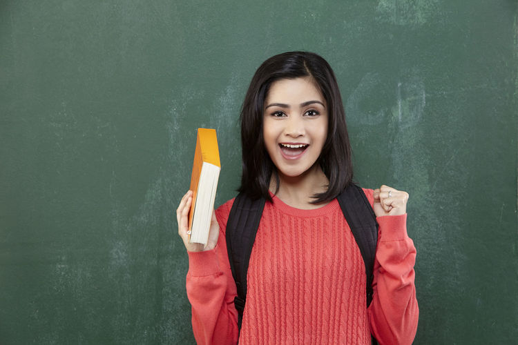 Portrait of cheerful female student gesturing while standing by blackboard