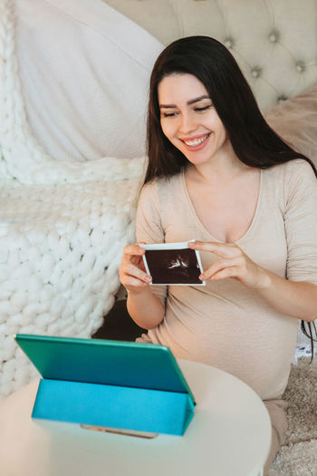 High angle view of pregnant woman showing ultrasound photographs during video call