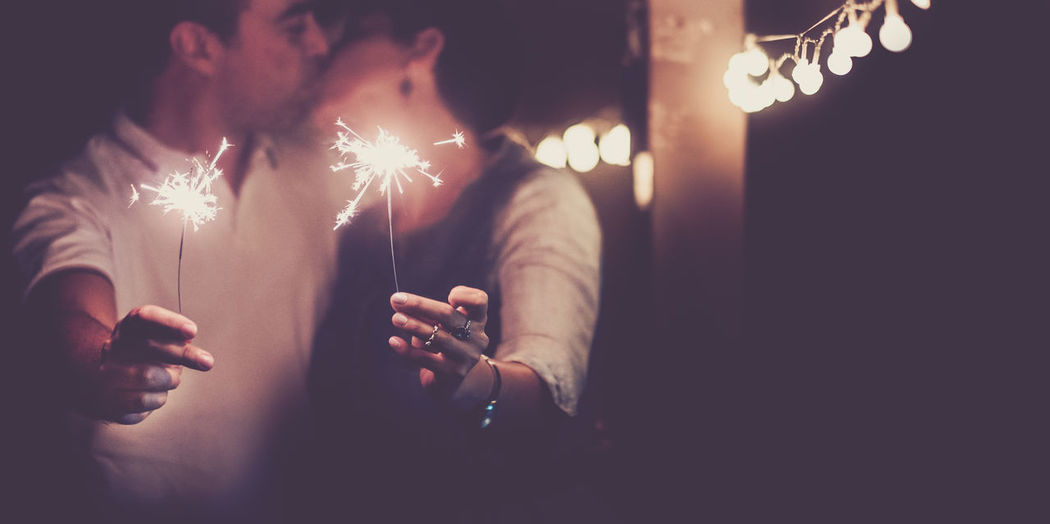 Couple kissing while holding sparklers at night