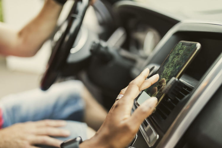 Hand of woman using gps through smart phone attached on dashboard in car