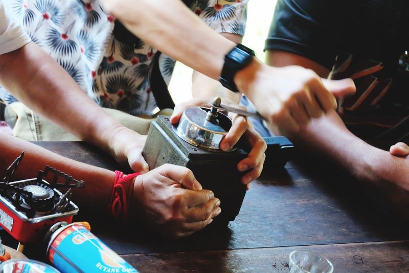 Midsection of people using coffee grinder on table