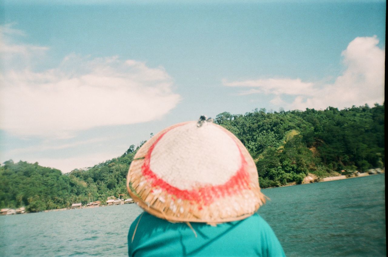 REAR VIEW OF WOMAN WEARING HAT AGAINST LAKE