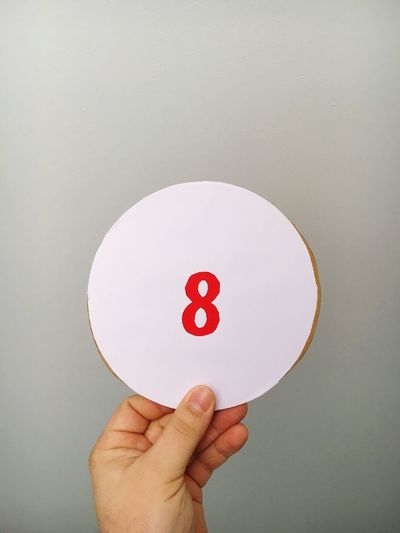 Cropped hand of person holding number on cardboard against gray background